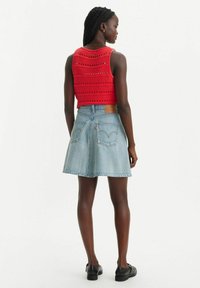 Haut court en tricot rouge avec un motif de mailles ouvertes, associé à une jupe en denim bleu clair en forme de A, dotée de poches arrière et d'une étiquette en cuir.