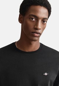 Black short-sleeve t-shirt with a crew neck, featuring a small embroidered logo on the chest. Smooth fabric texture.