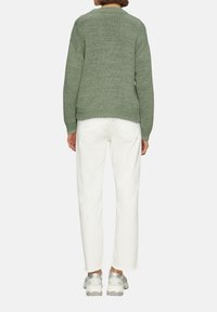 Pull en maille verte à coupe décontractée, avec des poignets et un ourlet côtelés, associé à un pantalon blanc et des baskets avec une semelle translucide.