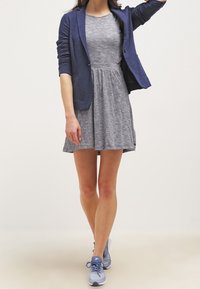 Granatowa marynarka na szarym sukience z rozkloszowanym dołem; jasnoniebieskie buty sportowe; gładki materiał; dopasowany krój; rękawy do połowy długości.