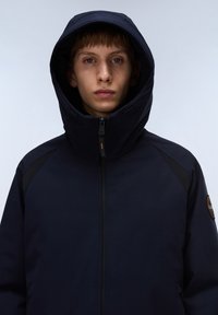 Chaqueta con capucha en color navy con cierre de cremallera, con paneles texturizados en los hombros y un emblema en la manga izquierda. Acabado mate, sin patrones visibles.