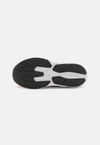 Semelle de chaussure de sport en caoutchouc noir avec un motif texturé et des accents blancs. Présente de larges rainures pour l'adhérence et la flexibilité.