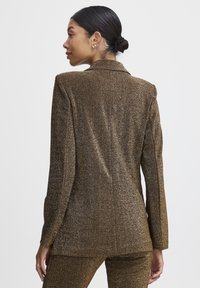 Braun metallischer Blazer mit texturierter Oberfläche, ausgestattet mit einem Reverskragen, taillierter Passform und langen Ärmeln. Die Rückansicht hebt klare Linien hervor.