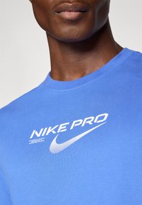 Blå bomull T-skjorte med rund hals, med "NIKE PRO" i hvit tekst og en hvit swoosh-logo, glatt tekstur og korte ermer.