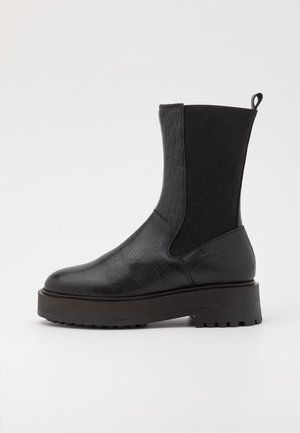 Bottine noire avec un motif crocodile texturé en cuir synthétique, côtés élastiques, languette et semelle en caoutchouc épaisse.