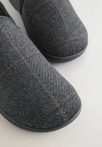 Papuci de culoare gri închis, fabricați din fetru texturat. Prezintă un model tartan subtil cu accente portocalii. Talpa din cauciuc negru asigură durabilitate.