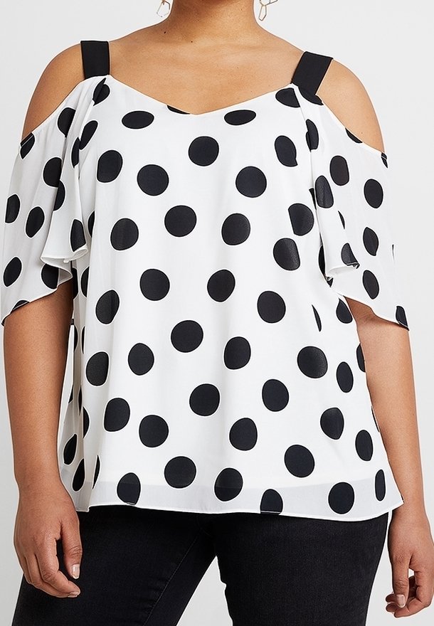 Donna che indossa una blusa bianca a spalle scoperte con pois neri e spalline nere, abbinata a pantaloni neri.