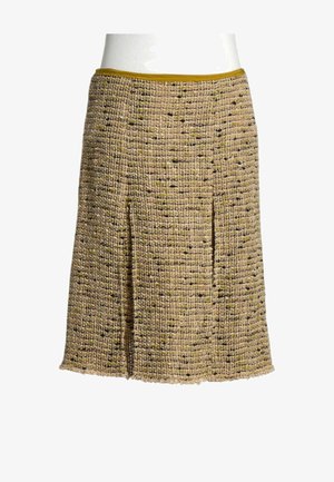 Jupe trapèze longueur genou en tweed beige texturé et noir avec des accents verts subtils, avec deux plis sur le devant et une ceinture jaune moutarde.