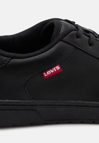 Baskets en cuir noir avec une finition texturée, bout rond, configuration à œillets pour les lacets, et logo Levi's rouge sur le côté.