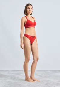 Czerwony bratlet i pasujące thongi wykonane z gładkiej tkaniny, z logo Calvin Klein na pasku. Prosty design o minimalistycznej estetyce.