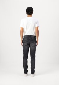 Jeans in denim nero con vestibilità slim e leggera scoloritura, abbinati a una t-shirt bianca semplice. Tasche posteriori in vista e cintura cucita.