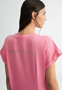 Růžové bavlněné tričko s krátkými rukávy, klasickým výstřihem a nápisem "WONDERFUL" ve třpytivém písmu na zadní straně. Hladká textura.