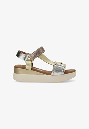 Sandalias metálicas en plata y oro con suela de plataforma, que presentan tiras entrecruzadas y un acabado texturizado. Cierre ajustable con hebilla.