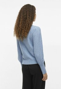Hellblaues Sweatshirt mit Zickzackmuster, geripptem Saum und Bündchen sowie leicht puffierten Ärmeln, getragen mit schwarzen Hosen. Sicht von hinten.
