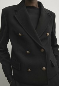 Musta kaksirivinen bleiseri jossa on tekstuuri kangas, kultaiset napit, lovetut kaulukset ja jäsennelty olkasuunnittelu.