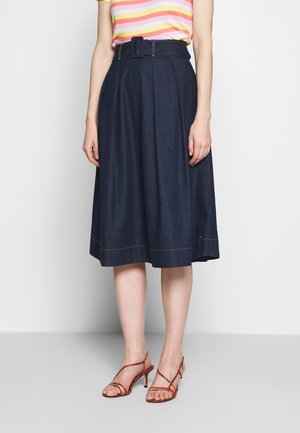 Denim-A-Linien-Rock mit Falten, dunkelblaue Farbe, breiter Gürtel mit Schnalle, mit kontrastierenden Nähten versehen. Kombiniert mit roten Riemchen-High-Heels.