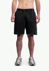 Czarne sportowe spodenki z elastycznym pasem, teksturowaną tkaniną i bocznymi szwami. Noszone z szarymi butami do biegania.