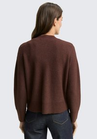 Brauner gerippter Pullover mit lockerer Passform, Rundhalsausschnitt und strukturierten Details an den Ärmeln. Kombiniert mit dunklen Jeans, die einen lässigen Stil zeigen.