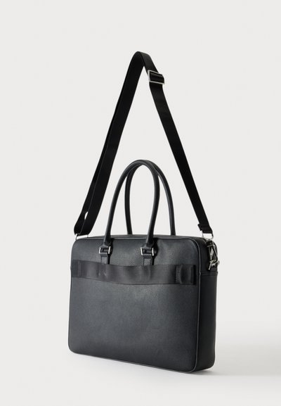 Serviette en cuir noir texturé avec deux poignées et une bandoulière réglable sur un fond uni clair.