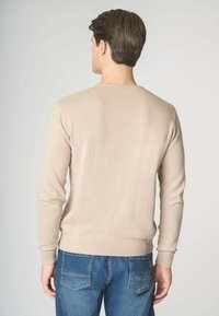 Maglione a maglia beige con scollatura rotonda e maniche lunghe, caratterizzato da polsini e orlo a coste. Indossato con jeans in denim blu.