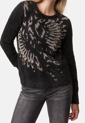 Czarny, puszysty sweter z abstrakcyjnym srebrnym wzorem orła, noszony z ciemnoszarymi jeansami, głowa modela częściowo widoczna.