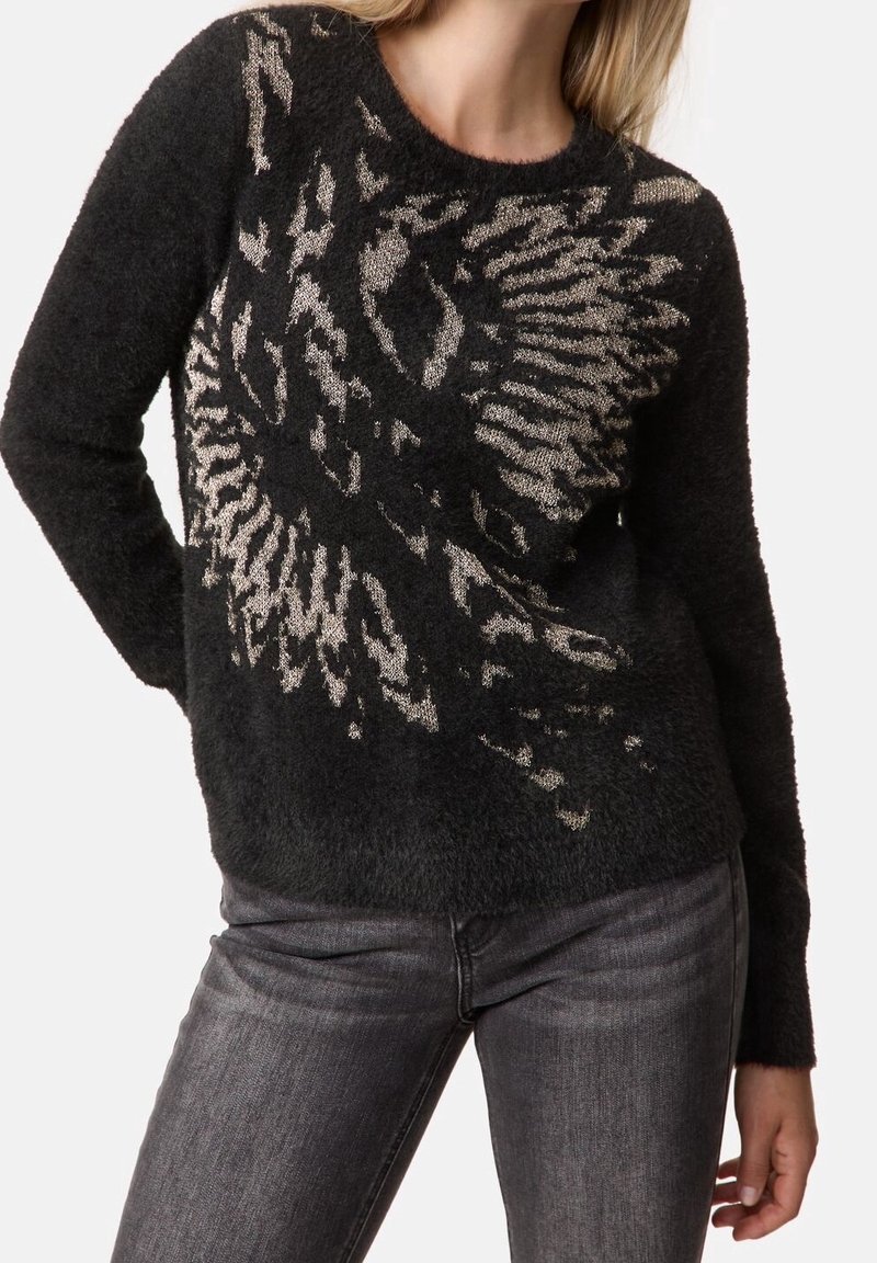 Pull noir duveteux avec motif abstrait d'aigle argenté porté avec un jean gris foncé, tête du modèle partiellement visible.