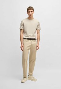 T-shirt beige à manches courtes associé à un pantalon beige, avec une ceinture noire et des baskets de couleur claire. Design simple et coupe décontractée.