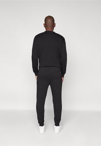 Svart sweatshirt og bukser med teksturert finish. Har tettsittende mansjetter og en subtil merkevarelogo bak på nakken. Hvite joggesko.