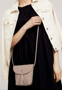 Borsa a tracolla finta pelle di un rosa chiaro, con chiusura a pattina e dettaglio con frange. Indossata sopra un vestito nero, con una giacca beige.