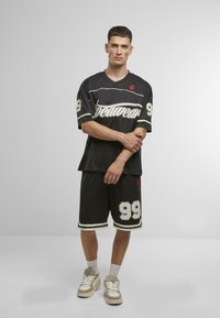 Fekete sportöltözet, amely rövidujjú mezből áll, fehér részletekkel és 99-es számmal, ugyanolyan színű rövidnadrággal és világos sportcipővel párosítva.