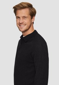 Zwarte gebreide poloshirt met een kraag en drie knopen, voorzien van geribbelde mouwen en een gestructureerde afwerking. Model zijwaarts weergegeven.