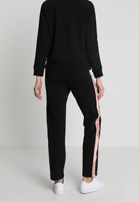 Czarna bluza z kieszeniami i pasującymi spodniami z różowymi bocznymi paskami z napisem "MAISON SCOTCH". Gładka dzianina bawełniana, luźny krój i długość do kostek.