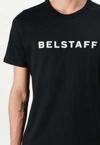 Black cotton t-shirt featuring a round neck andshort sleeves. The front displays the white logo "BELSTAFF" in bold text.