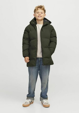 Grønne polstrede jakke med hætte og hel lynlås, båret over en lysfarvet skjorte, parret med blå jeans og beige sneakers.