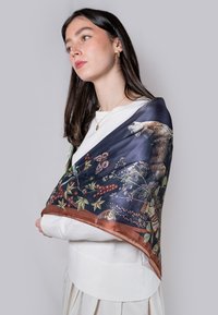 Foulard en soie avec un fond bleu foncé orné de motifs animaliers et floraux, bordé de marron. Léger avec une texture lisse.