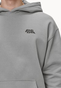 Jasnoszara bluza z kapturem z kieszenią kangurka i małym czarnym logo na lewej piersi. Wykonana z miękkiego materiału o luźnym kroju.