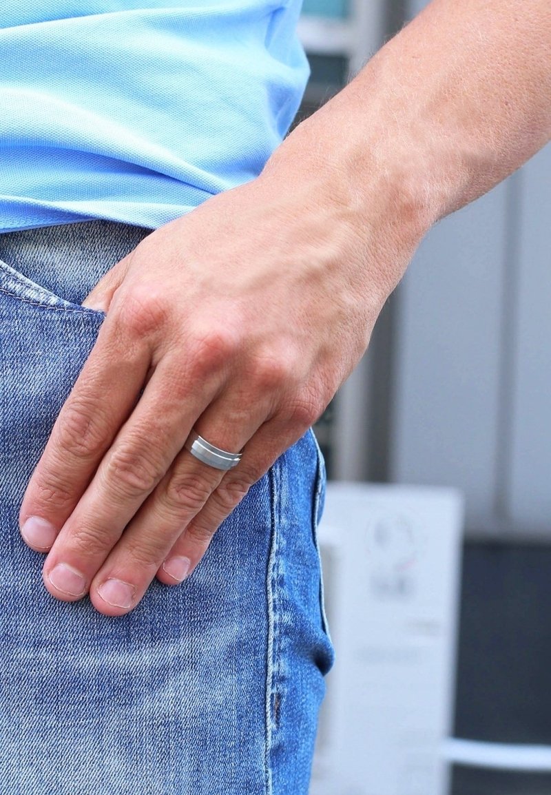 Titanium ring with two horizontal grooves, worn on the right hand. Hand resting on denim jeans, showcasing a natural skin texture.