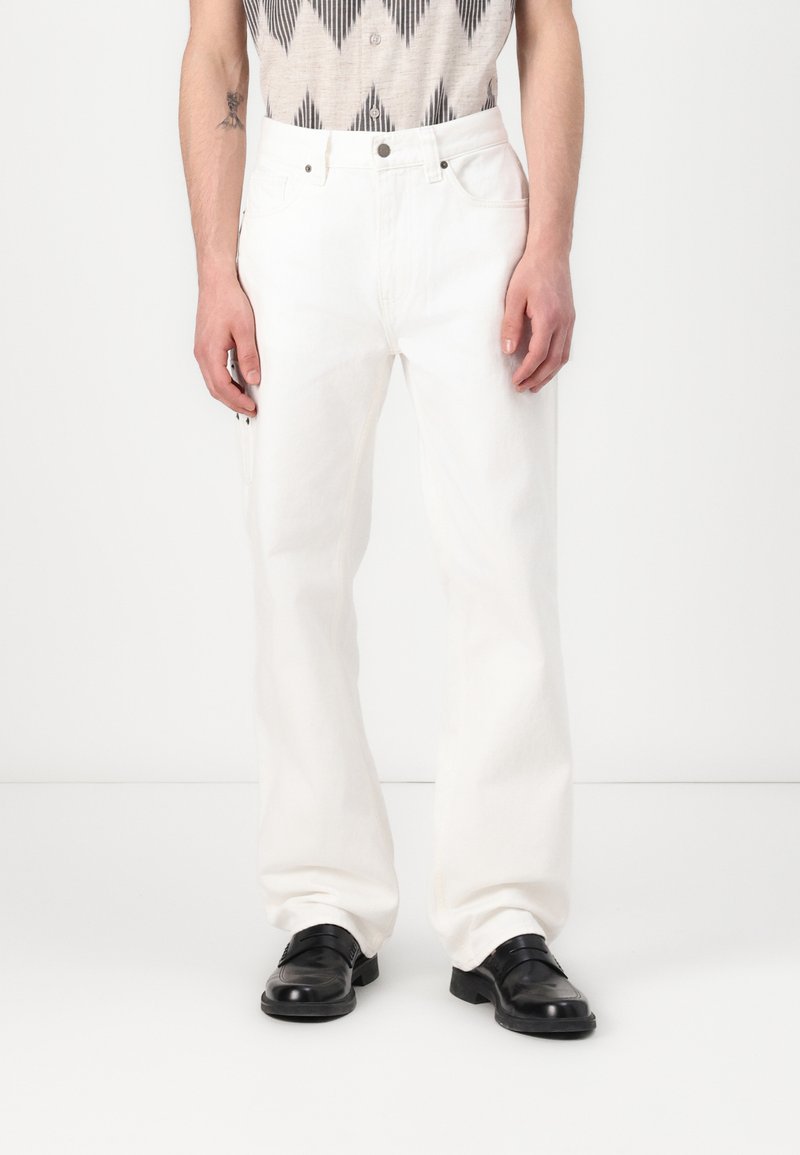 Witte denim broek met een rechte pasvorm, voorzien van vijf zakken en zichtbare stiksels. Gecombineerd met zwarte leren schoenen.