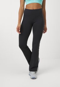 High-waisted black flared leggings made of stretch fabric, featuring a smooth texture and a fitted silhouette, paired with grey athletic shoes.