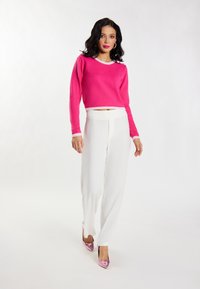 Maglione cropped rosa brillante con bordi bianchi, abbinato a pantaloni bianchi a gamba larga e tacchi rosa lucidi, creando un aspetto moderno e vivace.