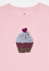 Rosa barntröja med ett paljettdekorerat cupcakesdesign som har vit glasyr och ett litet rött hjärta ovanpå.