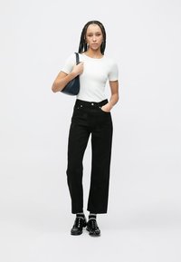 Melns džinsa plašu kāju bikses ar priekšējām kabatām, kombinētas ar piegulošu balto T-kreklu. Aksesuāri: tumša somiņa un spīdīgi melni apavi.