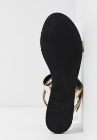 Svart sula med ribbad textur, med ett guldmetallicremdesign. Klacken är platt med en slät undersida. Storlek markerad som 39.