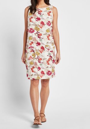 Robe sans manches mi-longue avec motif floral multicolore et poches devant, portée avec des sandales marron cloutées.