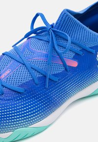 Scarpa sportiva blu con tomaia in rete, chiusura con lacci e design a gradiente. Presenta una superficie testurizzata e suola in gomma con accentuazione turchese.