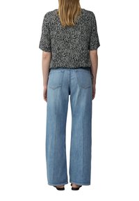 Haut noir à motifs à manches courtes avec une coupe décontractée, associé à un jean à taille haute et jambes larges de couleur bleu clair. Vue arrière montrant deux poches arrière.