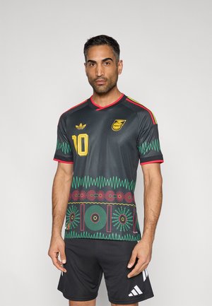 Mann iført svart fotballdrakt med fargerike geometriske mønstre, nummer 10, og svarte shorts, står foran en ensfarget lys bakgrunn.