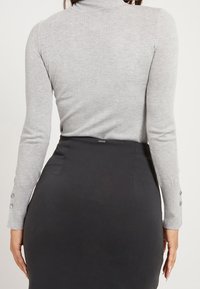 Grijze coltrui met geribbelde textuur, lange mouwen met knoopaccenten, gecombineerd met een zwarte getailleerde rok.