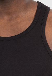 Schwarzes Baumwoll-Top ohne Ärmel mit einem runden Ausschnitt, das über eine glatte Textur und minimale Nähte verfügt, designed für Komfort und Bewegungsfreiheit.