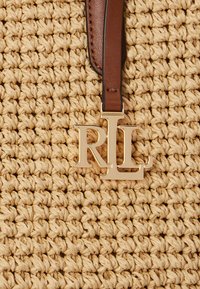 Pšenična tkanina torba s teksturiranim dizajnom. Ima smeđi kožni remen i zlatni detalj s logotipom "RL".